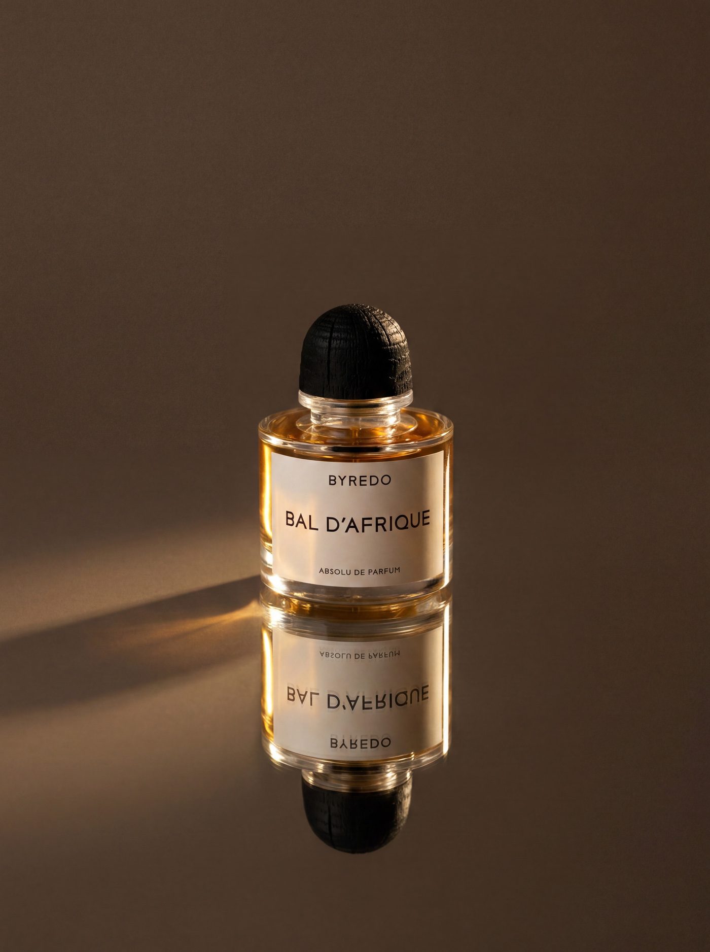 A gold capped fragrance bottle standing on a polished brown surface with its reflection