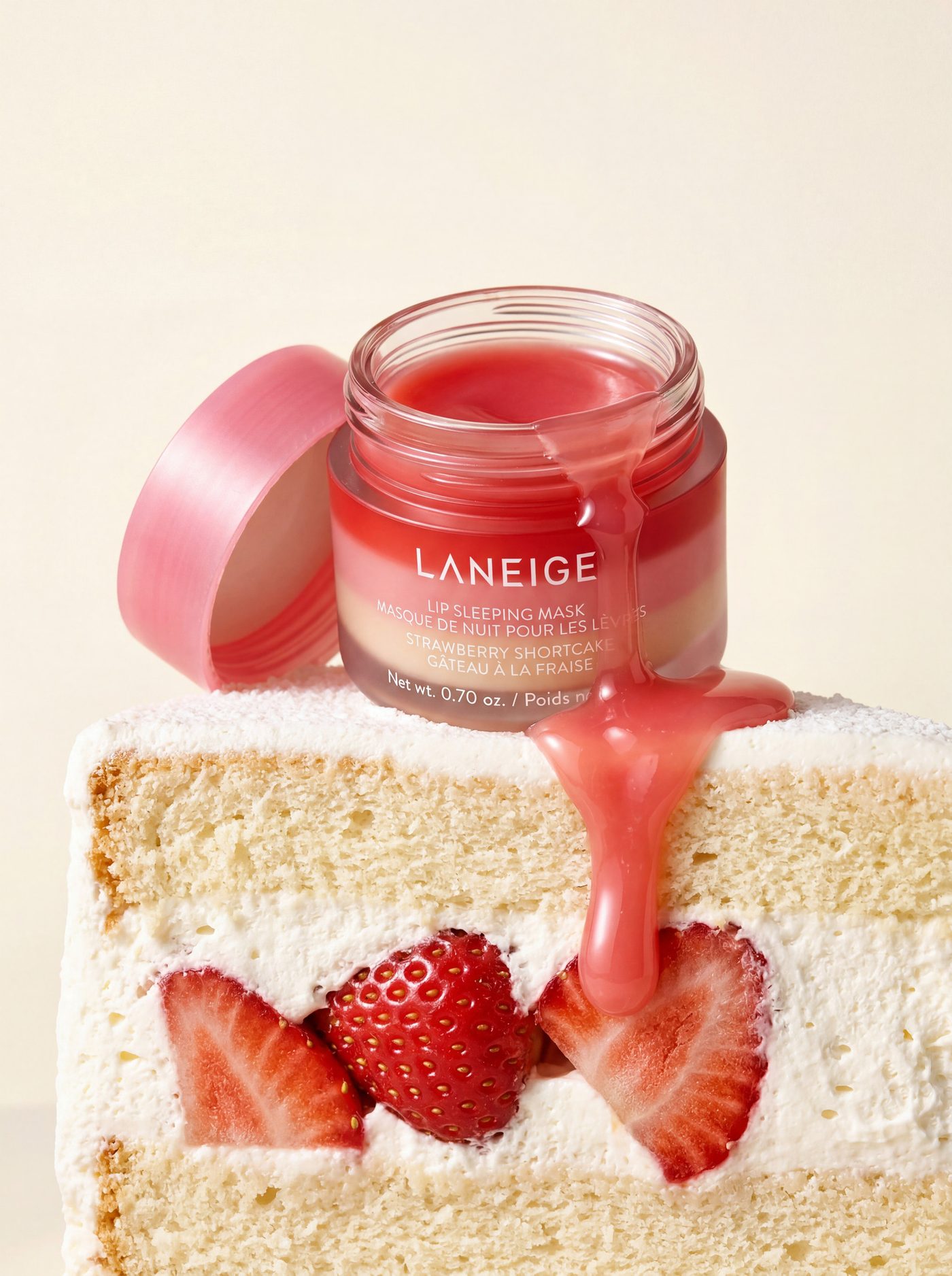 A beauty jar tipped over a slice of strawberry sponge cake, cream running down the layers