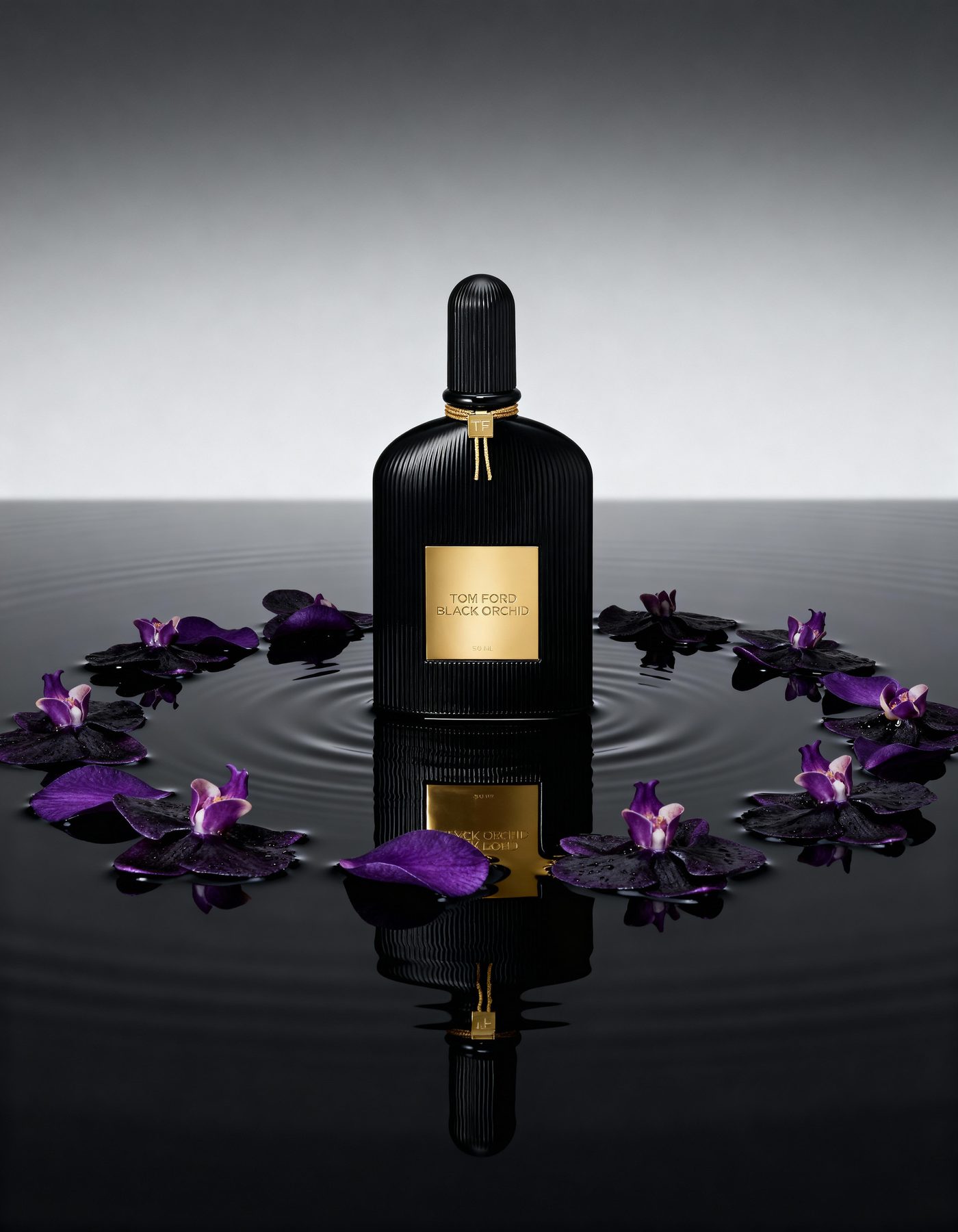A black fragrance bottle on a grey ground encircled by violet petals