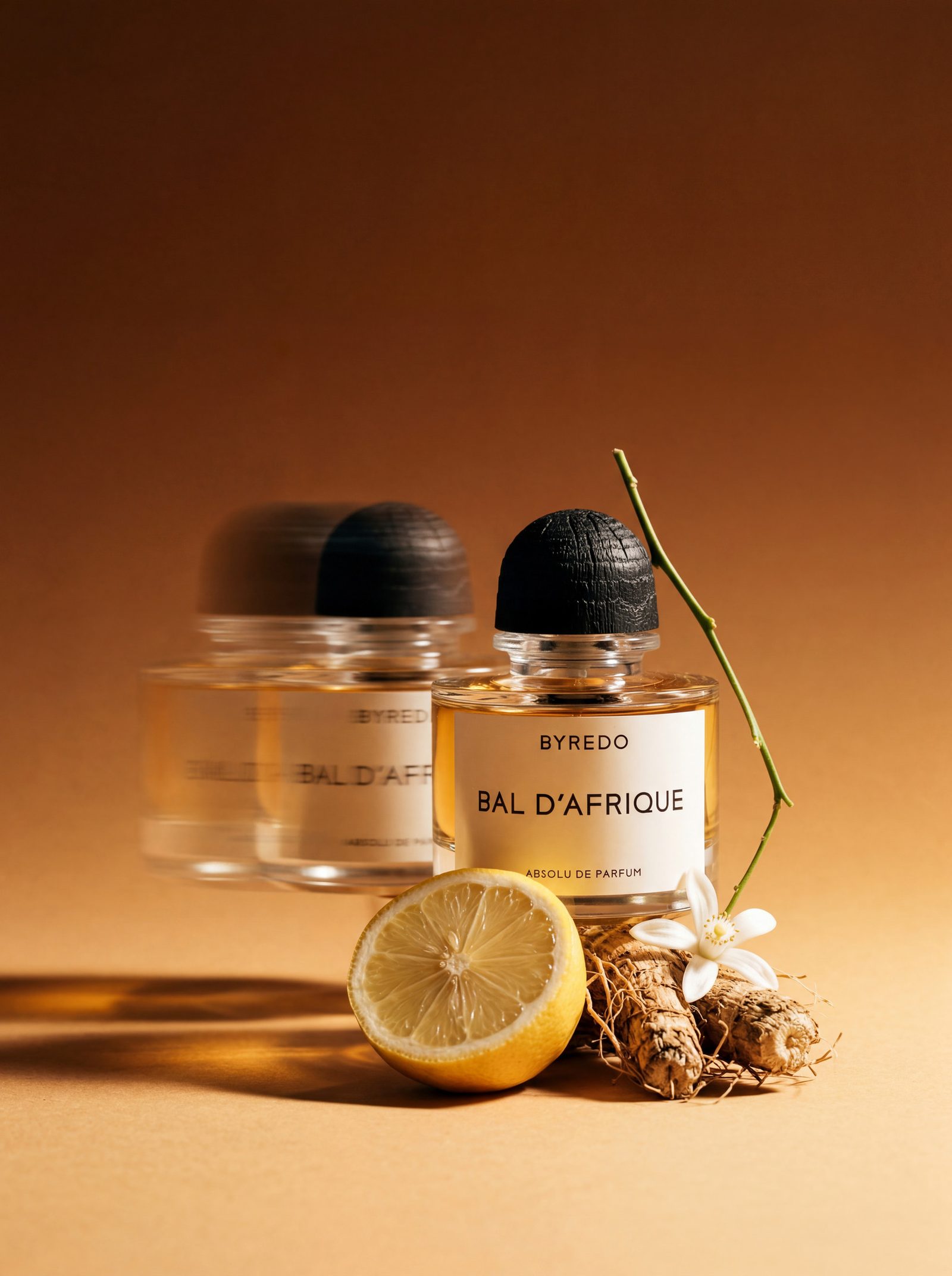 Two dark fragrance bottles on an amber ground with a halved lemon and dried ginger root